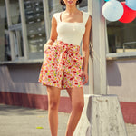 Woman in a white top and high waist red striped shorts standing outdoors with balloons in the background