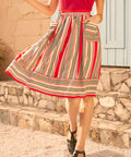 Person wearing a red top and colorful striped skirt standing outdoors.