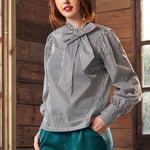 Woman wearing a striped blouse with a bow tie in front of a wooden wall.