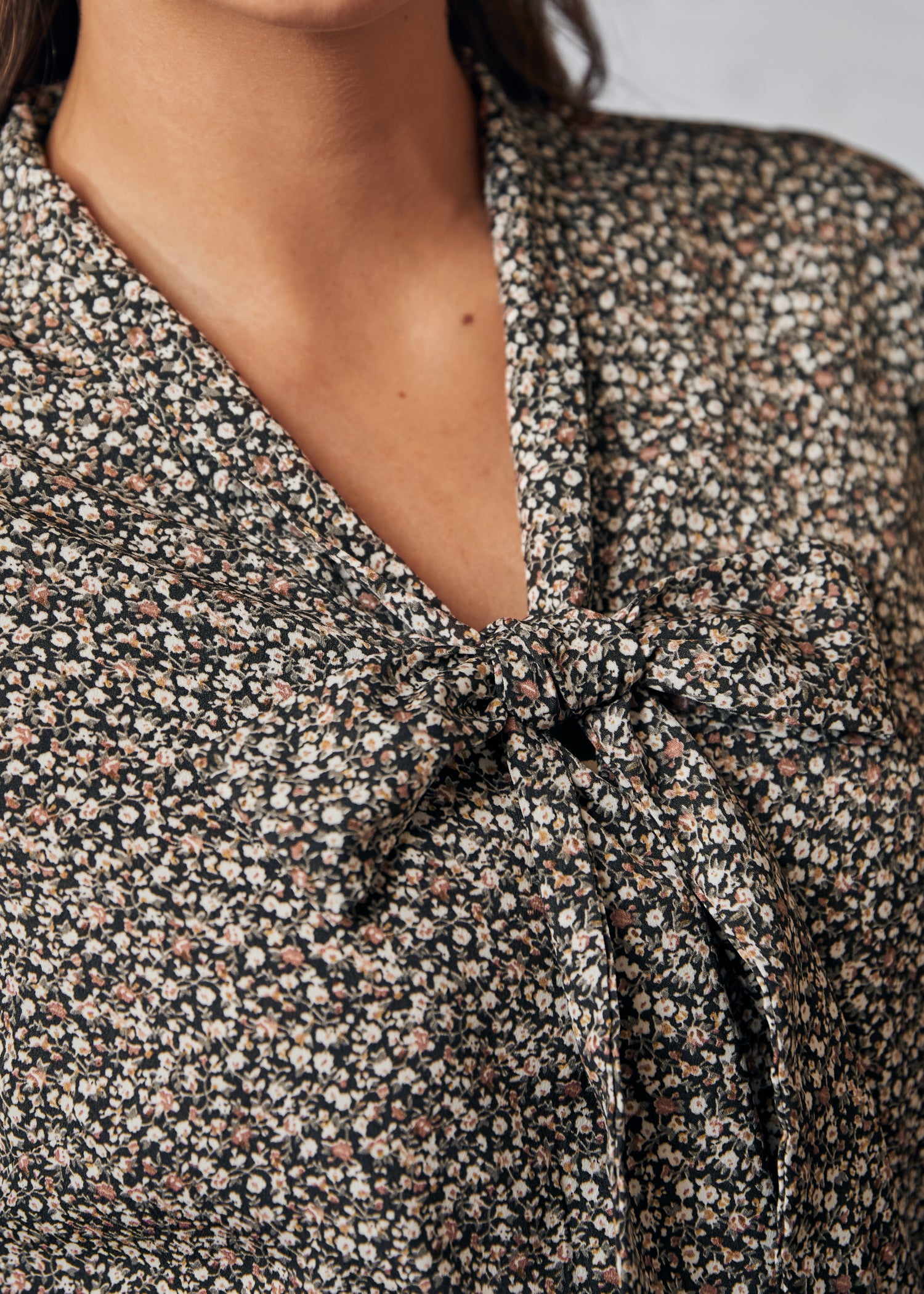 Close-up of a floral blouse with a knot detail on a neutral background