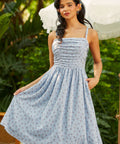Woman wearing a blue patterned dress standing outdoors with greenery in the background