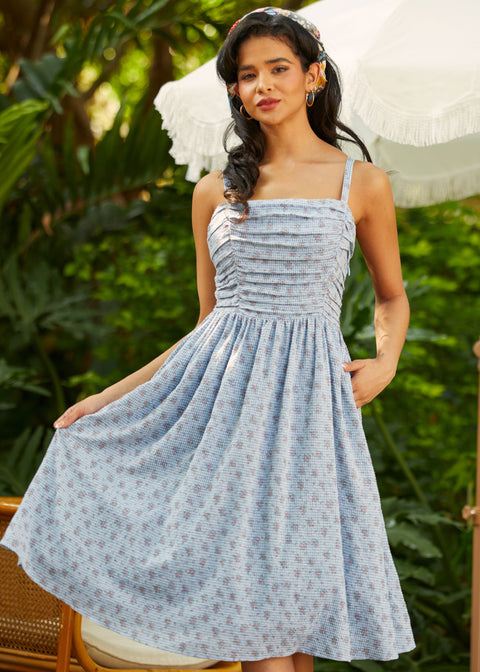 Woman wearing a blue patterned dress standing outdoors with greenery in the background