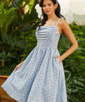 Woman wearing a blue patterned dress standing outdoors with greenery in the background
