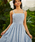 Woman wearing a blue patterned dress standing outdoors with greenery in the background