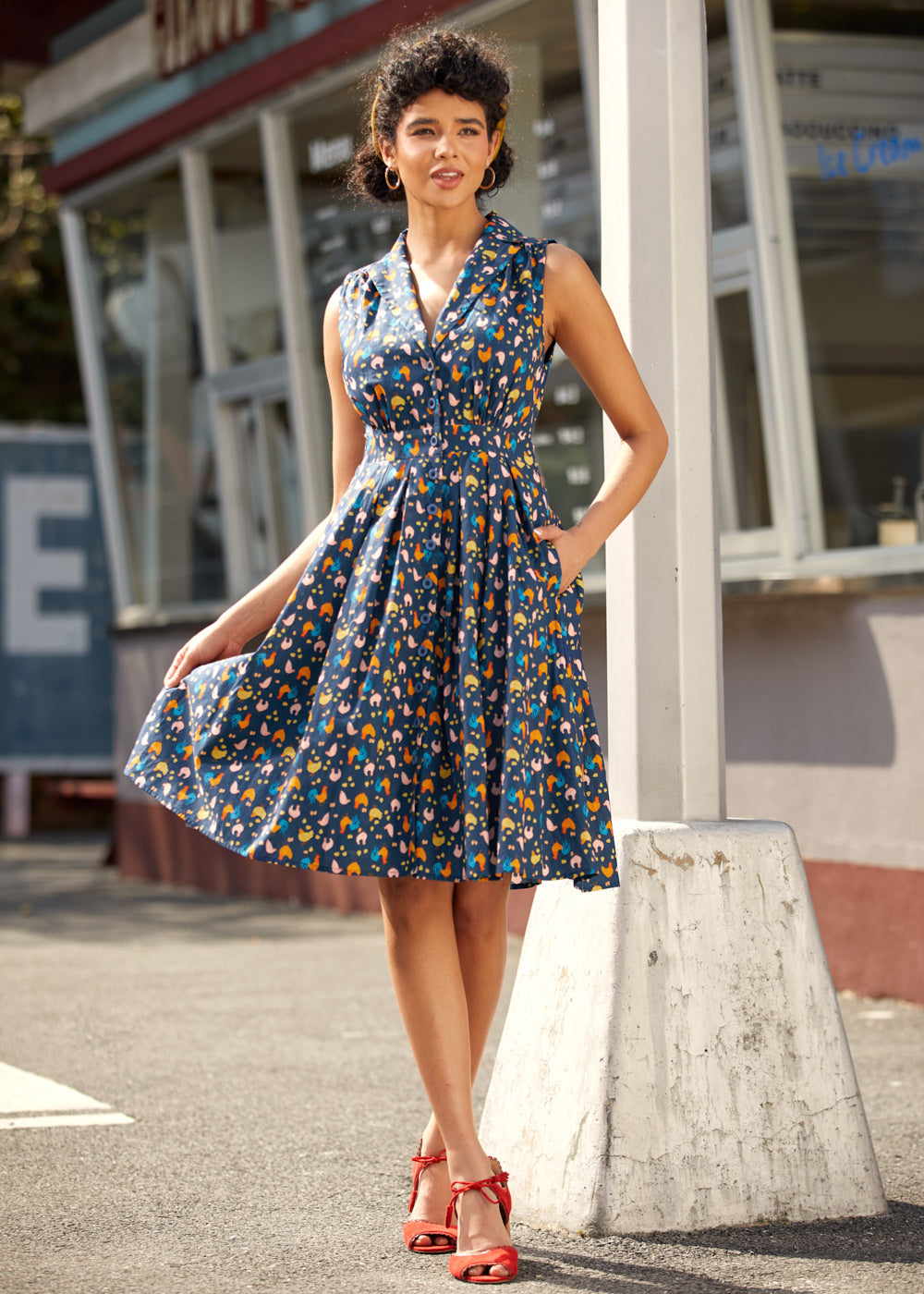 Woman wearing a sleeveless dress with a colorful chicken print and fit-and-flare silhouette.