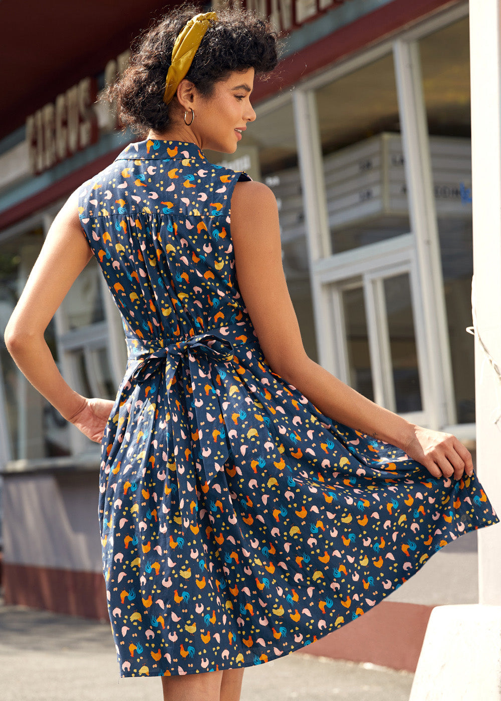 Back view of a farmyard chicken print dress with self-tie sash and novelty farmyard print.