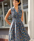 Woman wearing sleeveless chicken print dress with button-front bodice, notched collar, and gathered skirt.