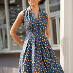 Woman wearing sleeveless chicken print dress with button-front bodice, notched collar, and gathered skirt.