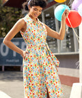 Woman in a colorful vegetable print dress holding balloons outdoors.