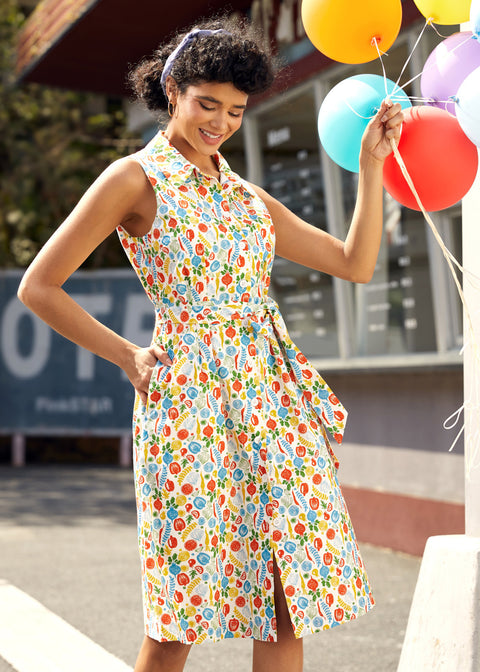 Woman in a colorful vegetable print dress holding balloons outdoors.
