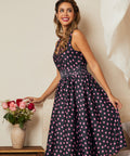 Woman wearing a navy blue dress with pink polka dots, holding flowers indoors.
