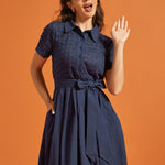 Woman wearing a retro-inspired fit-and-flare dress with an eyelet upper, smooth skirt, and side pockets.