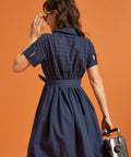 Back view of a navy shirt dress showing the eyelet-embroidered upper bodice, cuffed sleeves, and self-tie waist.