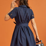 Back view of a navy shirt dress showing the eyelet-embroidered upper bodice, cuffed sleeves, and self-tie waist.