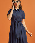 Woman wearing a navy fit-and-flare shirt dress with an eyelet bodice, pointed collar, and tie waist.