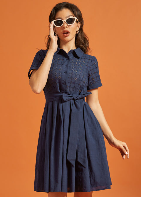 Woman wearing a navy fit-and-flare shirt dress with an eyelet bodice, pointed collar, and tie waist.