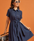 Front view of a navy cotton shirt dress featuring an eyelet bodice, pointed collar, and waist sash.