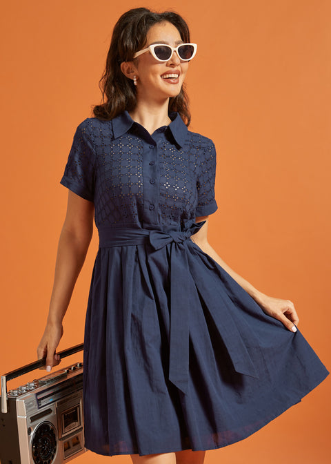 Front view of a navy cotton shirt dress featuring an eyelet bodice, pointed collar, and waist sash.