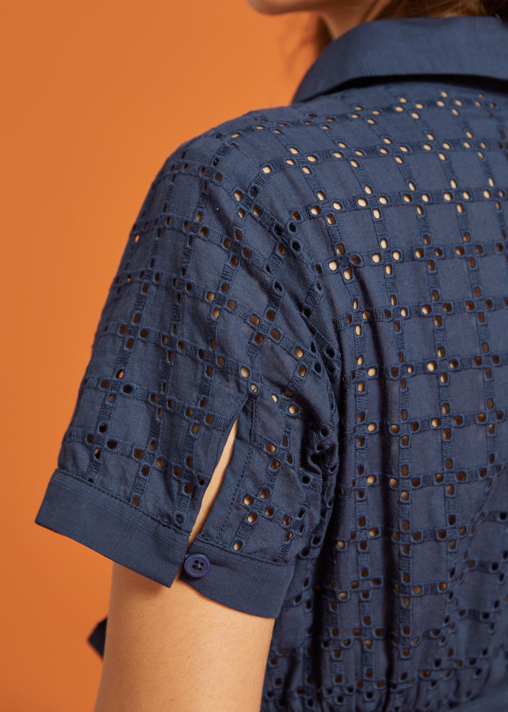 Close-up of the eyelet-embroidered short sleeve with cuff and button-tab slit detail.
