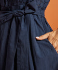 Detail of the removable self-tie sash, gathered skirt, and side pocket on a navy cotton dress.