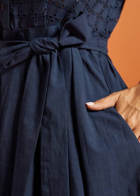 Detail of the removable self-tie sash, gathered skirt, and side pocket on a navy cotton dress.