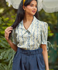 Woman wearing a floral blouse and navy pants with a blurred green background