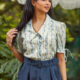 Woman wearing a floral blouse and navy pants with a blurred green background