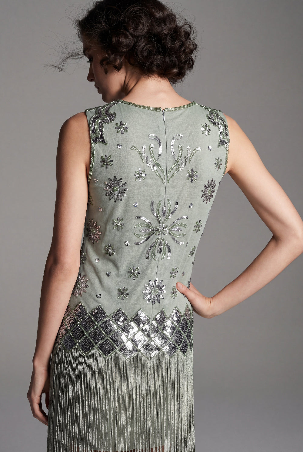Woman wearing a green dress with floral patterns and fringe details on a gray background