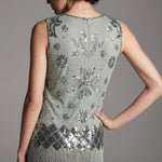 Woman wearing a green dress with floral patterns and fringe details on a gray background