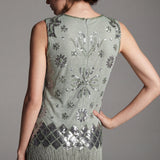 Woman wearing a green dress with floral patterns and fringe details on a gray background
