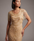 Woman wearing a gold beaded dress with fringe details against a gray background