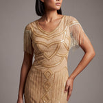 Woman wearing a gold beaded dress with fringe details against a gray background
