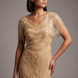 Woman wearing a gold beaded dress with fringe details against a gray background