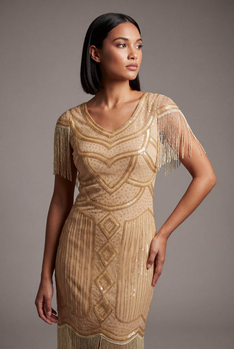 Woman wearing a gold beaded dress with fringe details against a gray background