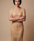Woman wearing a gold flapper dress with fringe details against a beige background