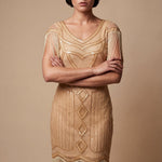 Woman wearing a gold flapper dress with fringe details against a beige background