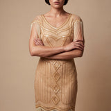 Woman wearing a gold flapper dress with fringe details against a beige background