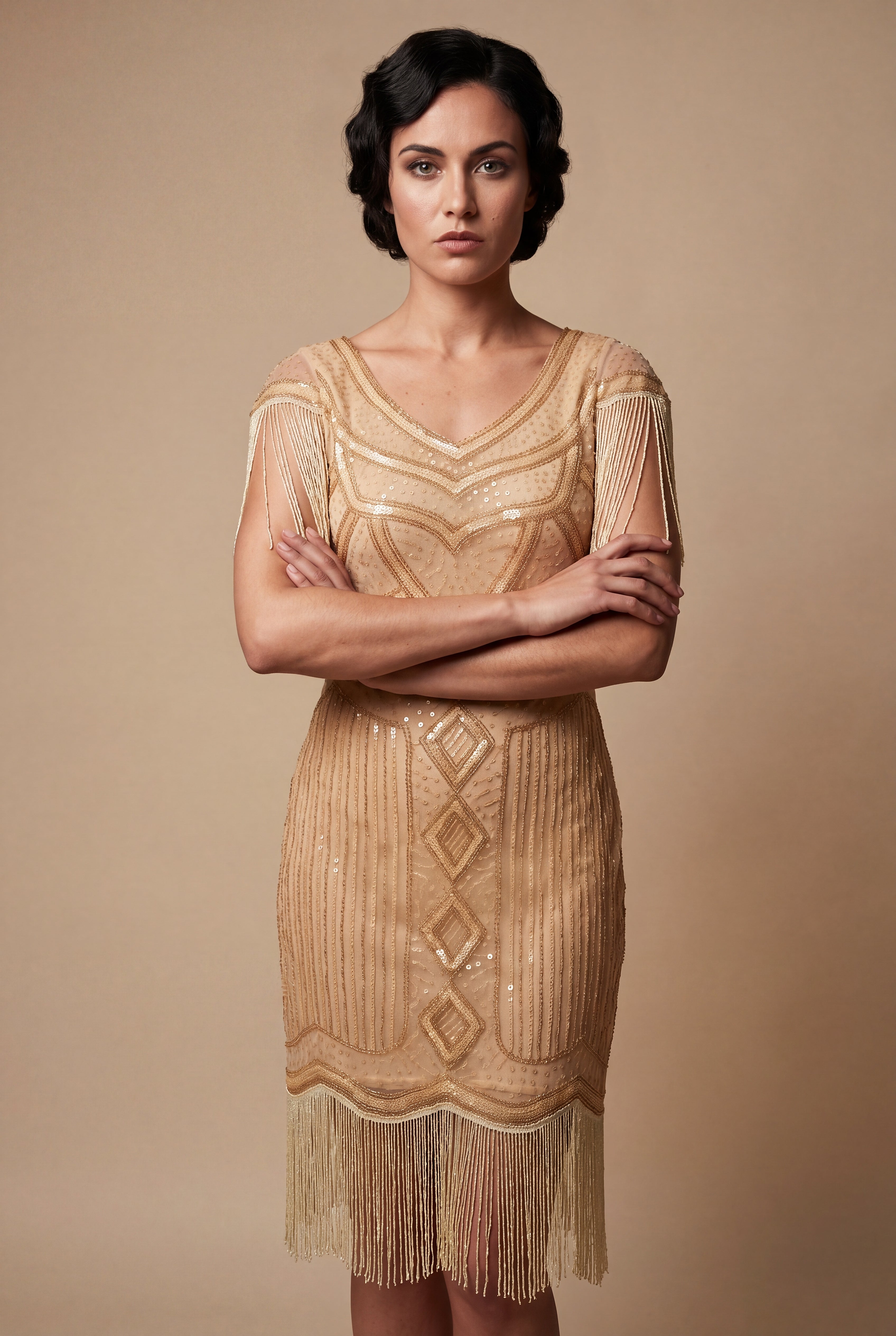 Woman wearing a gold flapper dress with fringe details against a beige background