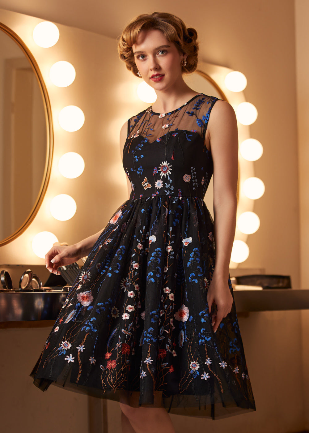 Woman wearing a sleeveless embroidered party dress with sheer mesh overlay and full vintage-inspired skirt.