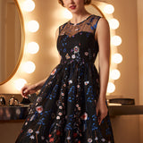 Woman wearing a sleeveless embroidered party dress with sheer mesh overlay and full vintage-inspired skirt.