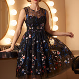 Woman wearing an elegant black floral embroidered cocktail dress with illusion yoke and twirl-ready silhouette.