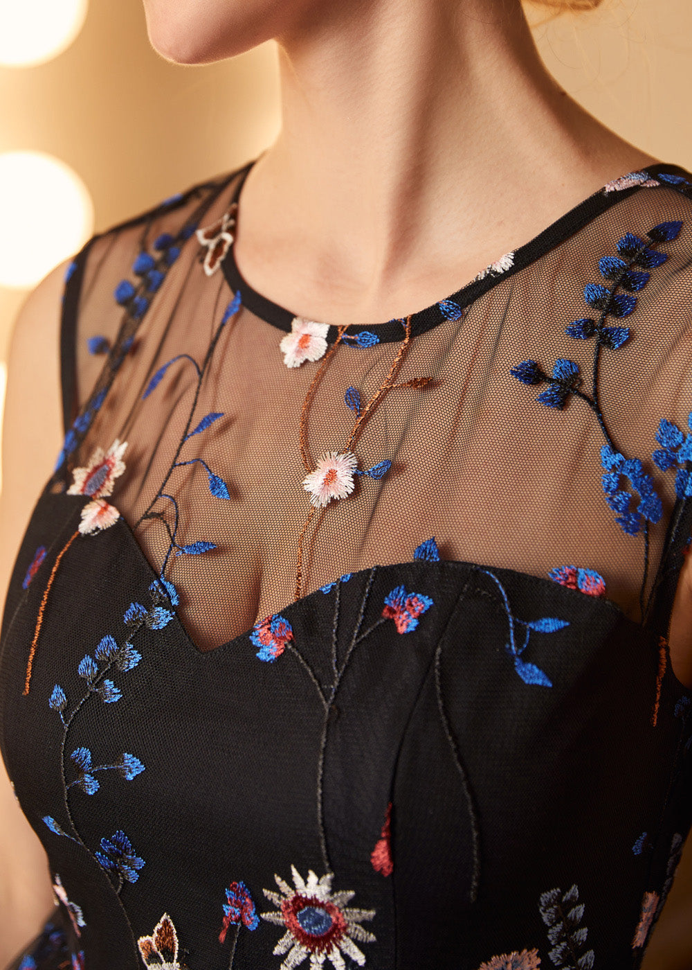 Close-up of the illusion mesh neckline with intricate blue floral embroidery and butterfly accents on a party dress.