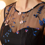 Close-up of the illusion mesh neckline with intricate blue floral embroidery and butterfly accents on a party dress.