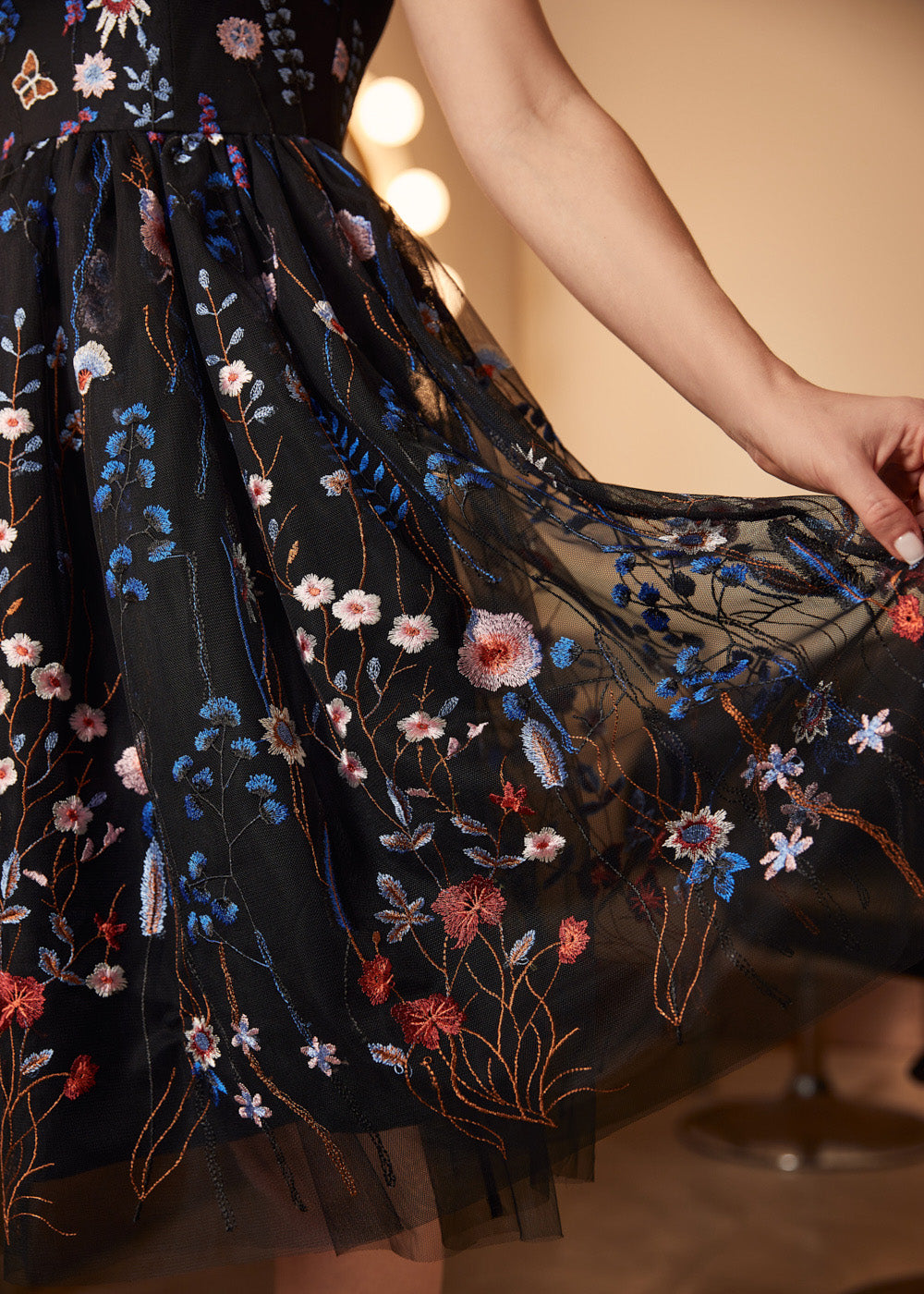 Detailed close-up of the embroidered mesh overlay with blue wildflowers, butterflies, and layered black tulle on a cocktail dress.