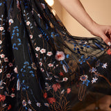 Detailed close-up of the embroidered mesh overlay with blue wildflowers, butterflies, and layered black tulle on a cocktail dress.