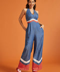 Woman wearing a blue wide-leg halter jumpsuit with retro chevron contrast details and side pockets.