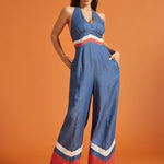 Woman wearing a blue wide-leg halter jumpsuit with retro chevron contrast details and side pockets.