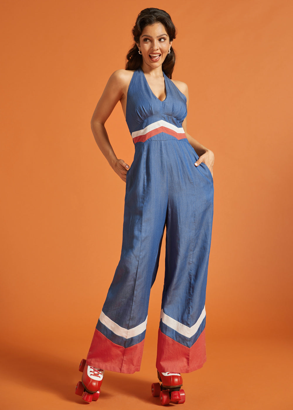 Woman wearing a blue wide-leg halter jumpsuit with retro chevron contrast details and side pockets.