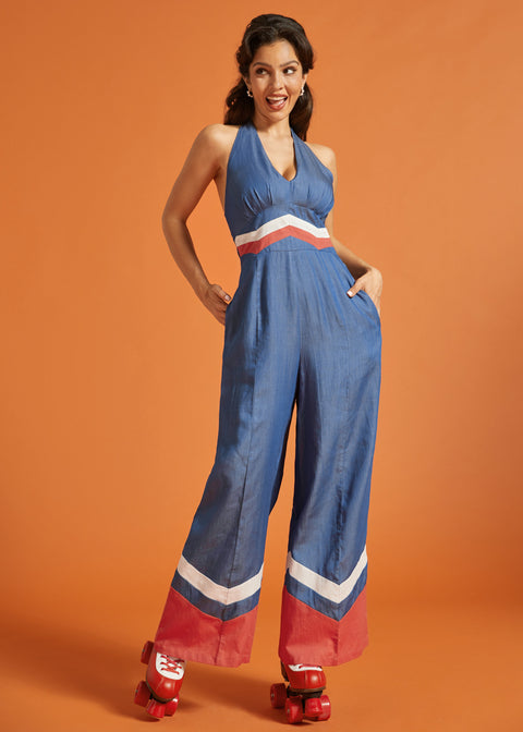 Woman wearing a blue wide-leg halter jumpsuit with retro chevron contrast details and side pockets.