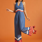 Woman wearing a retro blue jumpsuit with halter tie neckline and wide-leg silhouette.